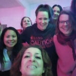 Eine Gruppe von zehn Frauen, die sich möglicherweise zum Tag der Alleinerziehenden oder zu einem Elternabend versammelt haben, lächeln und posieren eng beieinander für ein Selfie in einem Innenraum mit rosa Beleuchtung und wirken glücklich und fröhlich.